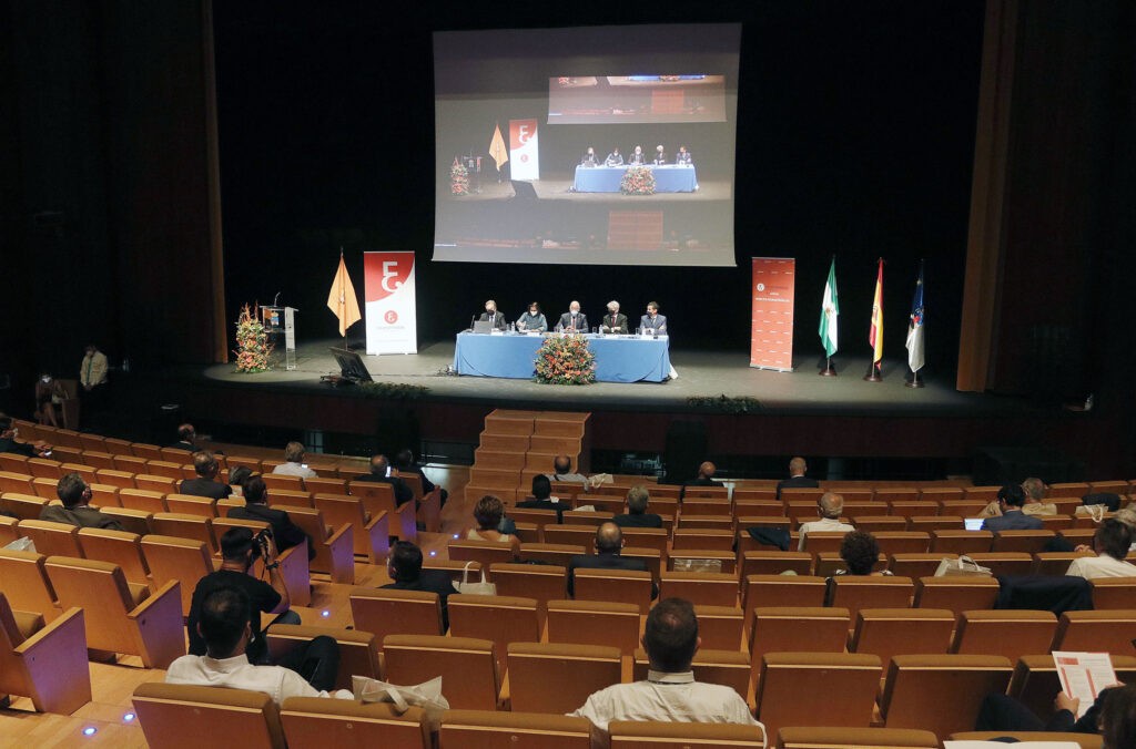 Congreso económico en auditorio con mesa redonda y asistentes