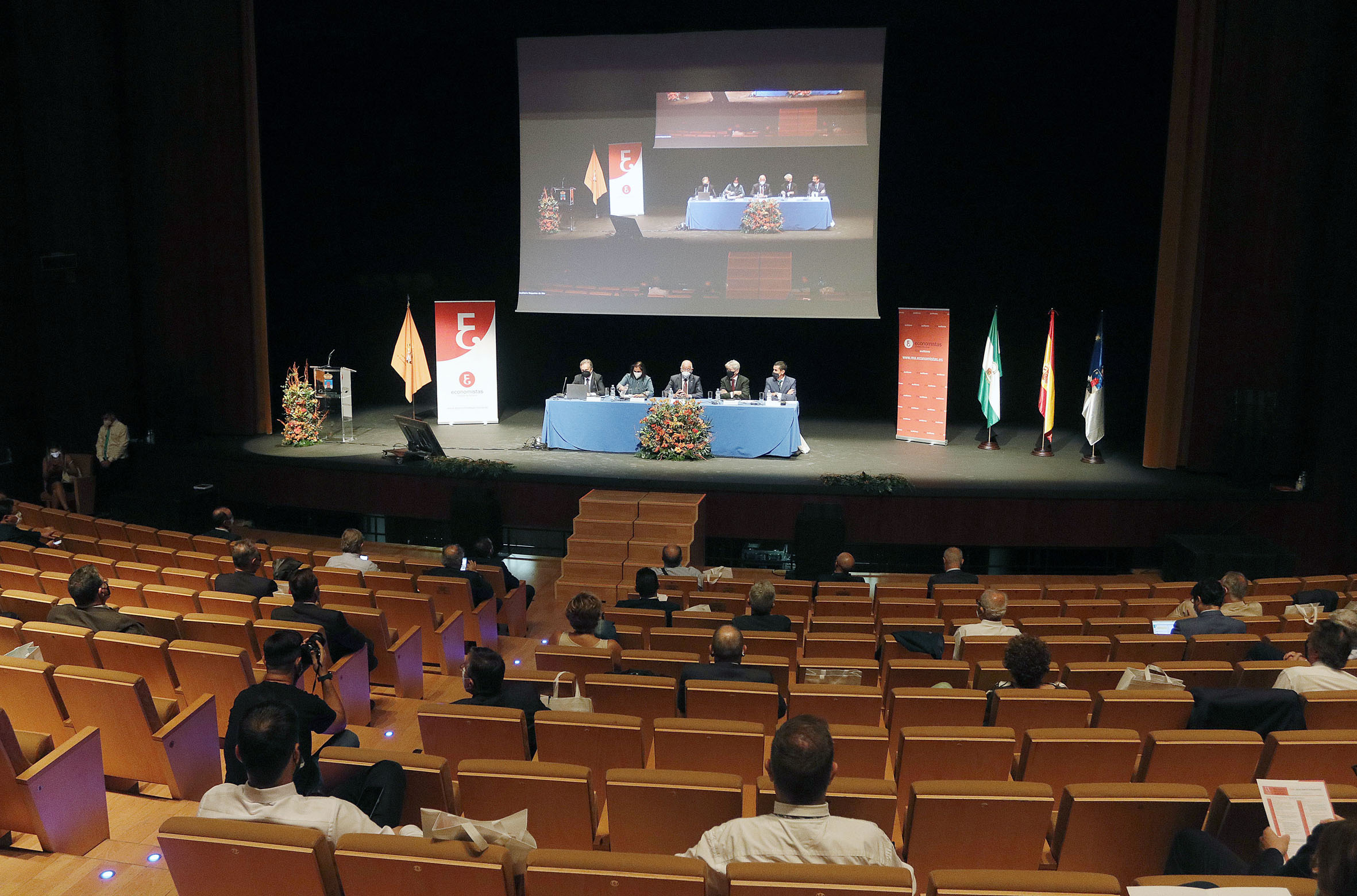 Congreso económico en auditorio con mesa redonda y asistentes