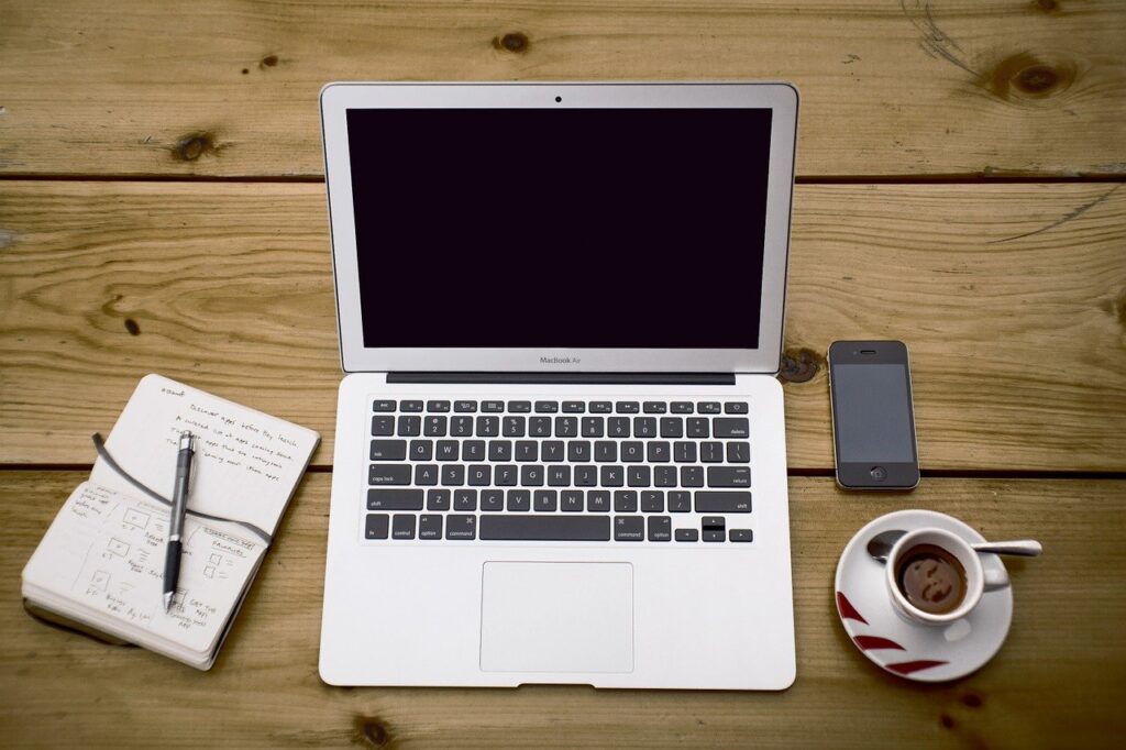 Foto de un portatil, movil, una libreta y un cafe sobre una mesa de madera